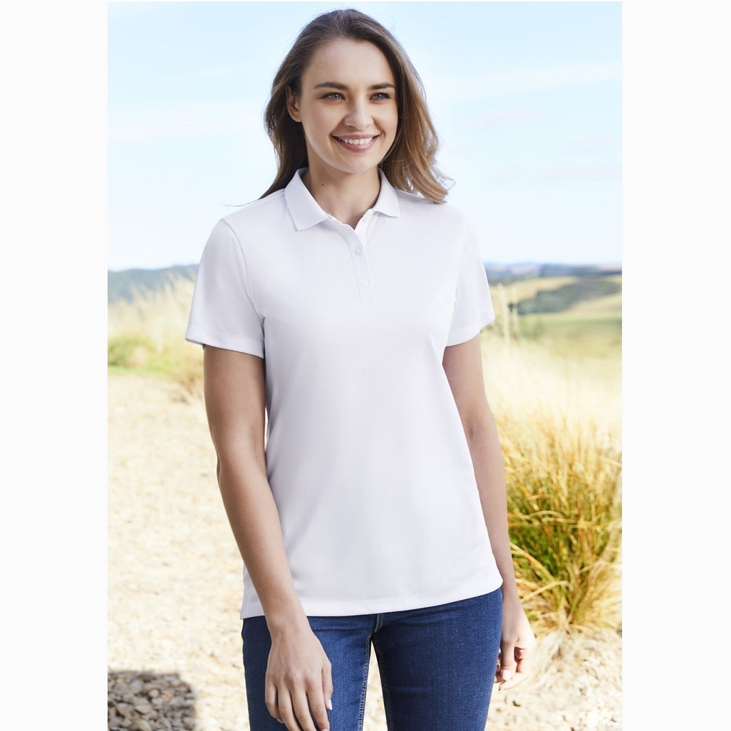 A woman wearing a white short sleeve polo shirt with a collar and pearlized buttons, standing outdoors.