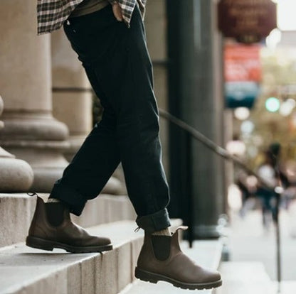 Person wearing brown Chelsea boots on stone steps with a blurred urban background