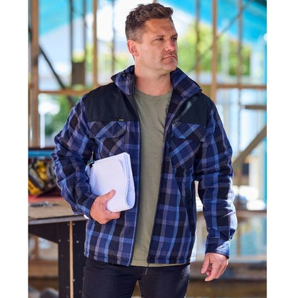 Man wearing a blue plaid jacket holding a white folder in an indoor setting.