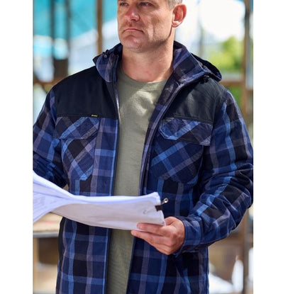 Man wearing a blue plaid jacket holding papers outdoors