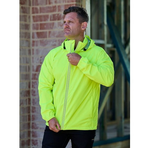 Man wearing a bright yellow jacket standing in front of a brick wall.