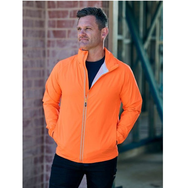 Man wearing an orange jacket standing against a brick wall.