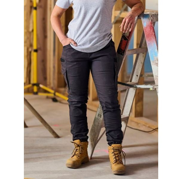 Person wearing black cargo pants and tan work boots standing next to a ladder in an industrial setting.