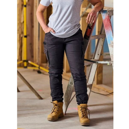 Person wearing black cargo pants and tan work boots standing next to a ladder in an industrial setting.