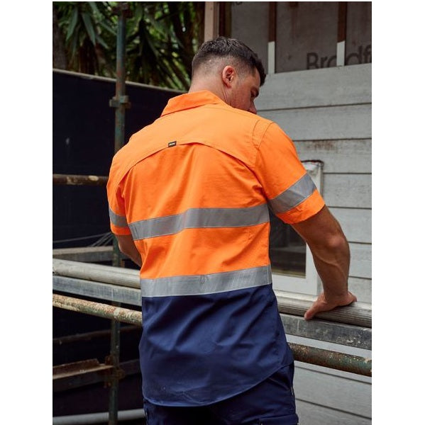 Person wearing an orange and navy work shirt with reflective stripes on a construction site.