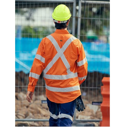 Person wearing an orange safety jacket with reflective stripes and a yellow hard hat on a construction site.