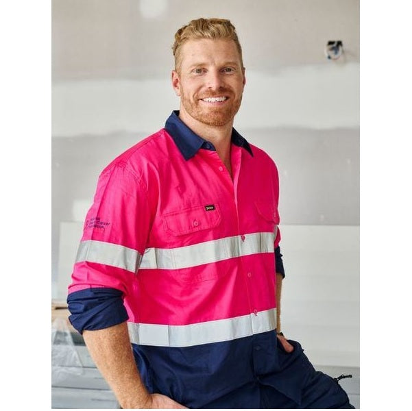 Man wearing a bright pink and navy work shirt with reflective stripes indoors.