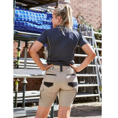 Person wearing a navy shirt and beige work pants in an outdoor setting with scaffolding and blue containers.