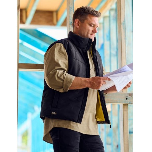 Man in a black vest holding papers in front of a window with blue light filtering through