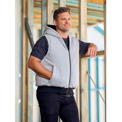 Man wearing a gray hooded vest standing against a blurred indoor background