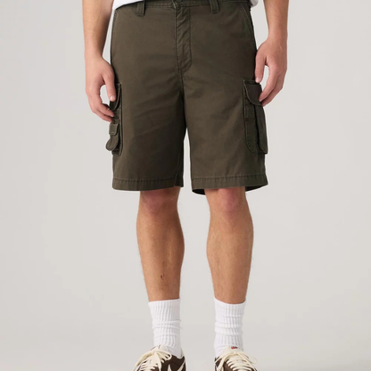 A person wearing olive green cargo shorts with side flap pockets, paired with white crew socks and brown sneakers, shown from the waist down against a light gray studio background.