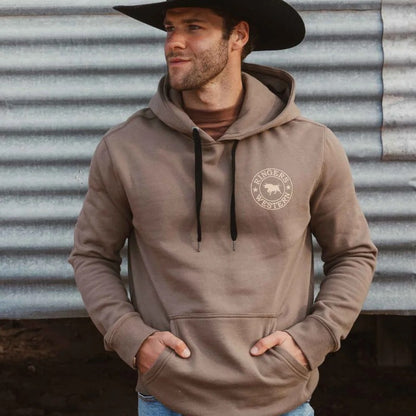 A man wearing a taupe-brown pullover hoodie with a circular 'Ringers Western' bull logo on the left chest, paired with a black cowboy hat in Australia outback