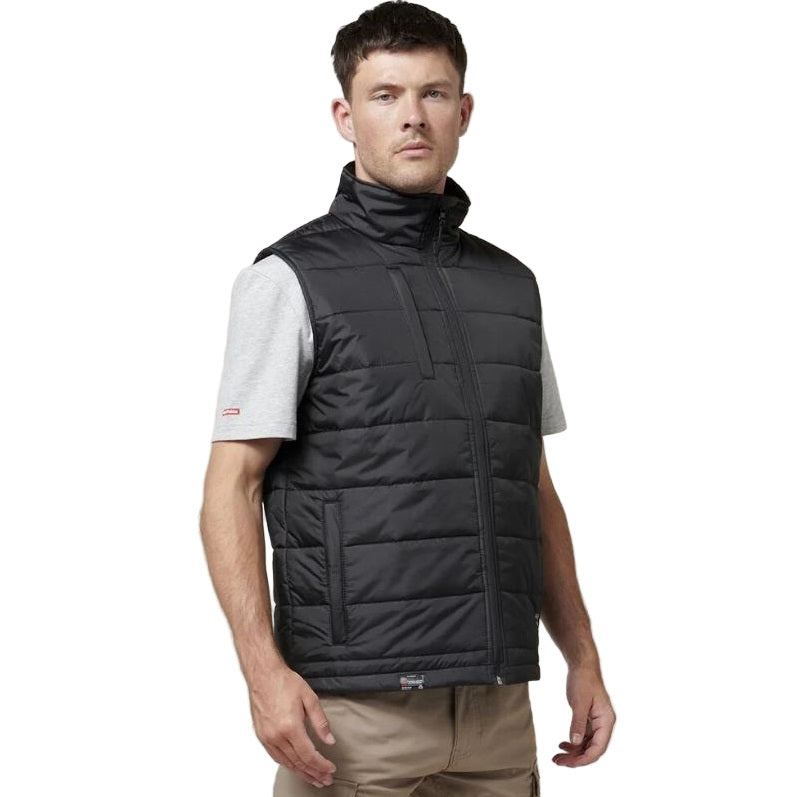 Man wearing a black puffer vest over a white shirt on a white background