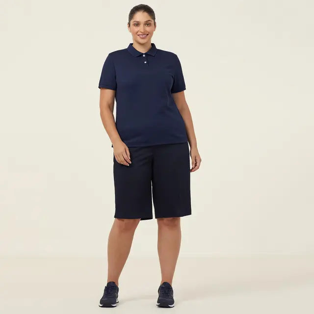 Woman wearing a navy blue polo shirt and shorts on a beige background