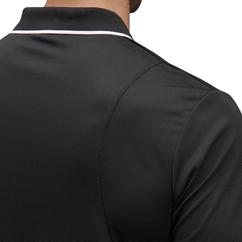 man wearing a black polo with white edge on collar one pocket and button down on white background.